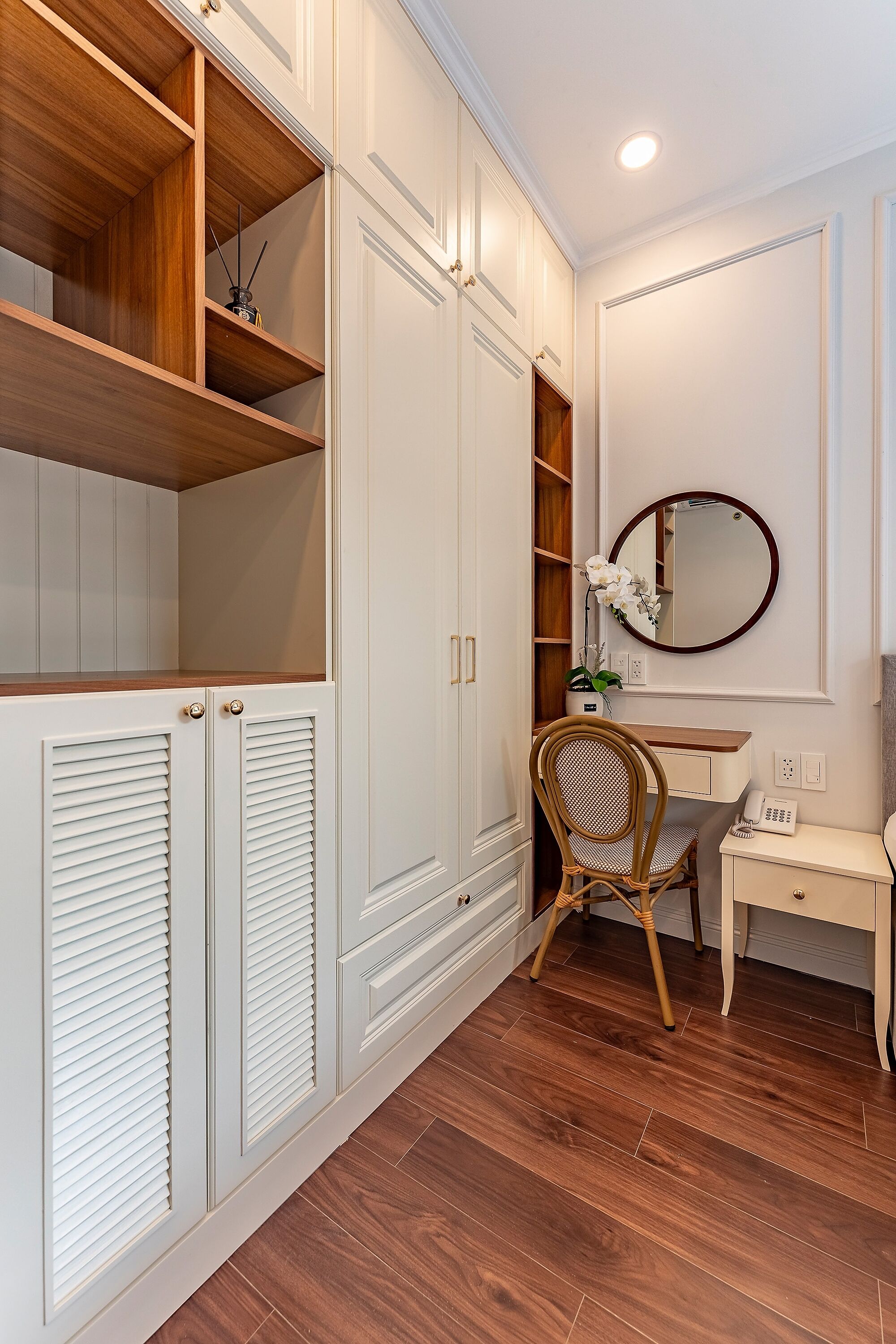 A room with a wooden floor, white cabinetry, a desk with a chair, and a mirror on the wall.