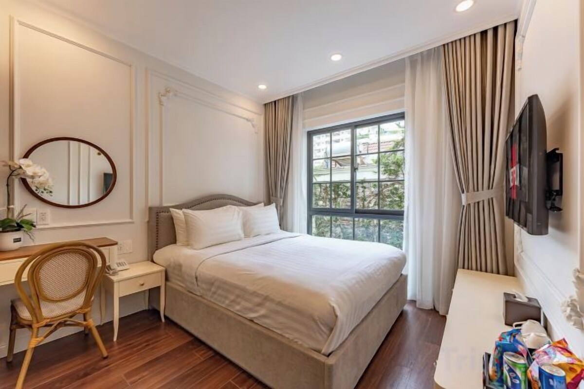 Habitación de hotel con cama, escritorio, silla, televisor y ventana con cortinas.