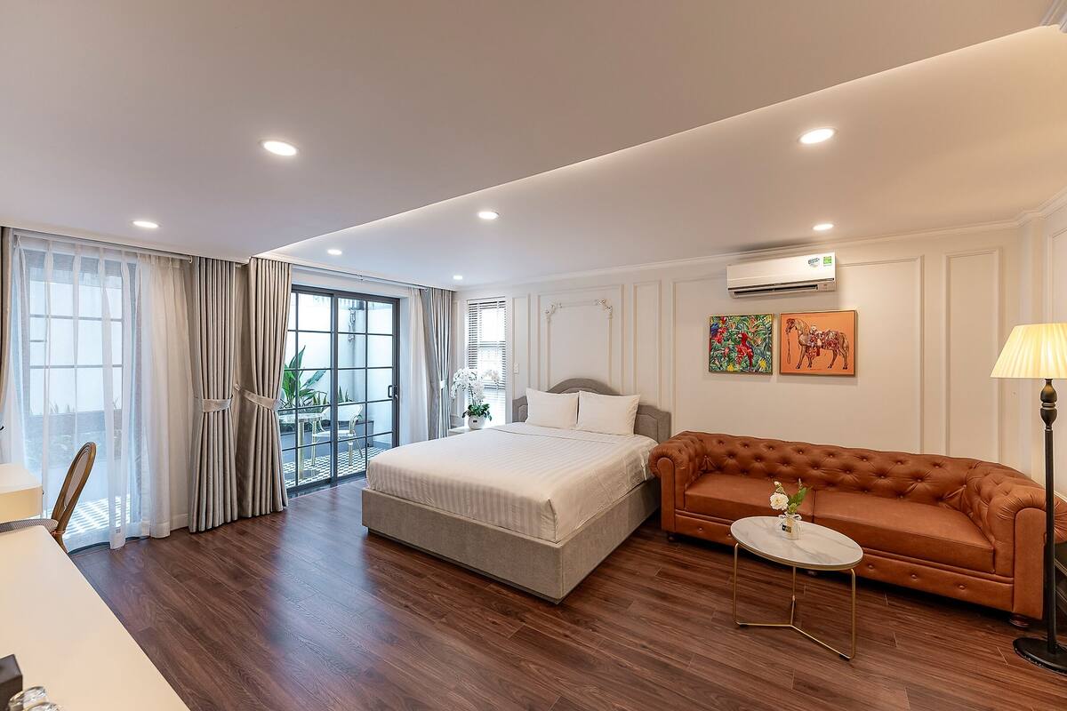 Ein modernes Hotelzimmer mit einem großen Bett, einer Couch, einem kleinen Tisch und Blick ins Freie.