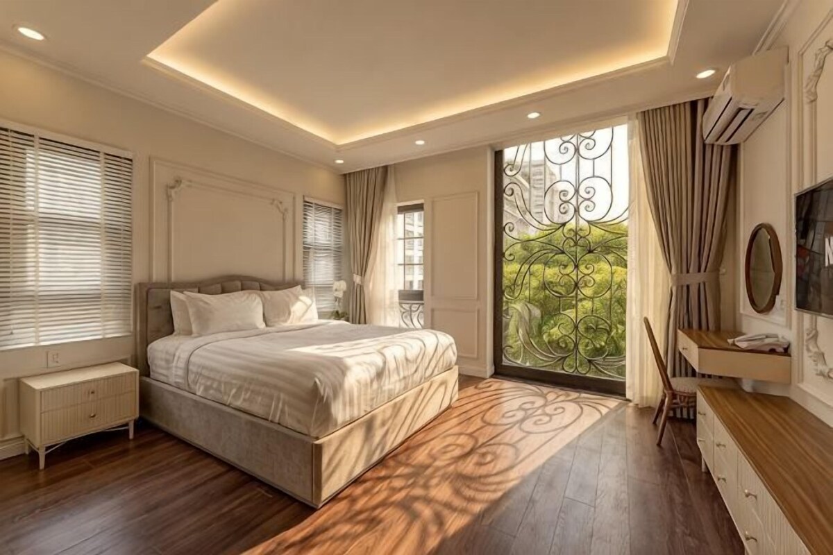 Een slaapkamer met een groot bed, een nachtkastje, een kaptafel, een televisie en een raam met gordijnen.