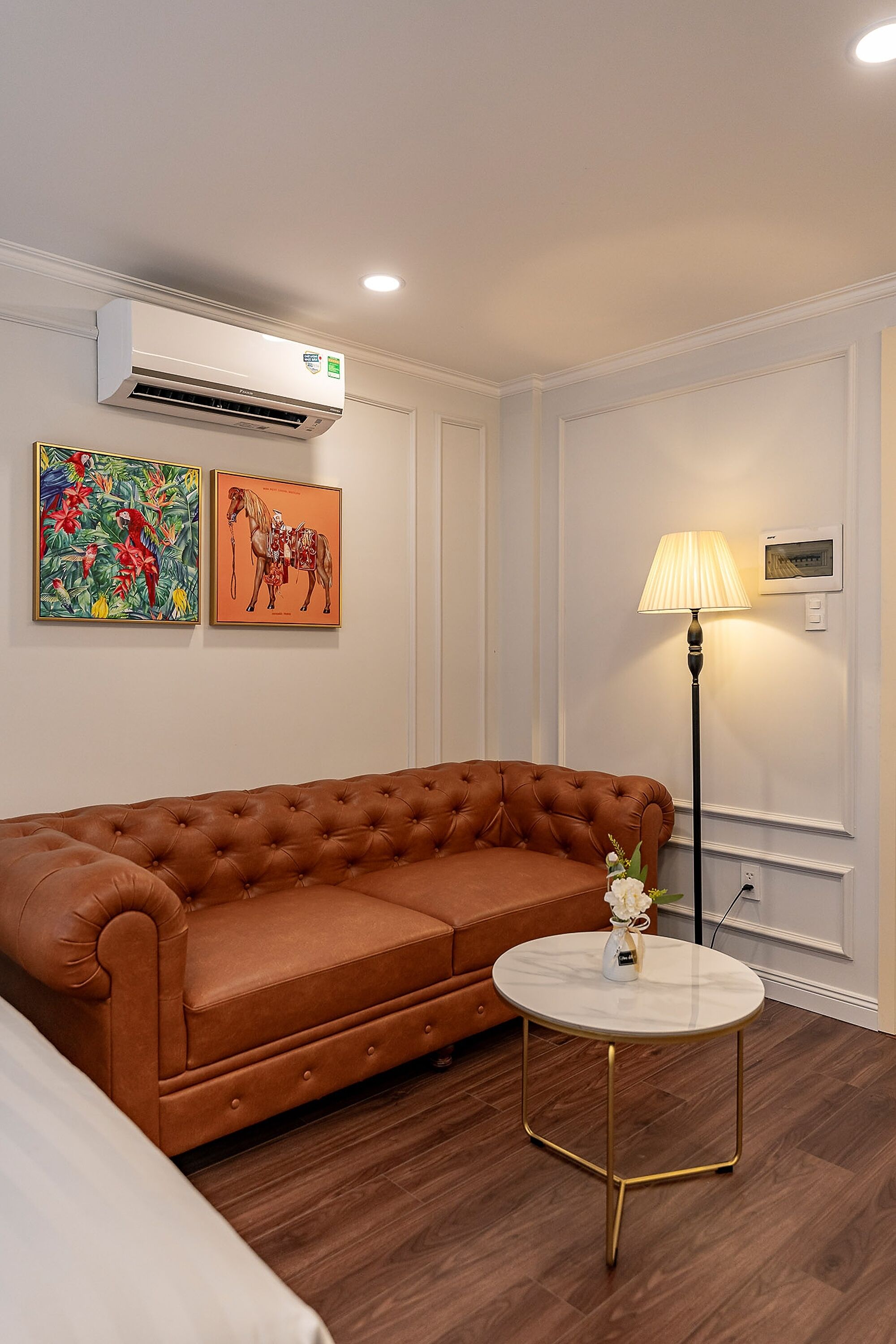 Ein Zimmer mit einem braunen Ledersofa, einem runden Tisch mit einer weißen Vase und zwei gerahmten Kunstwerken an der Wand.