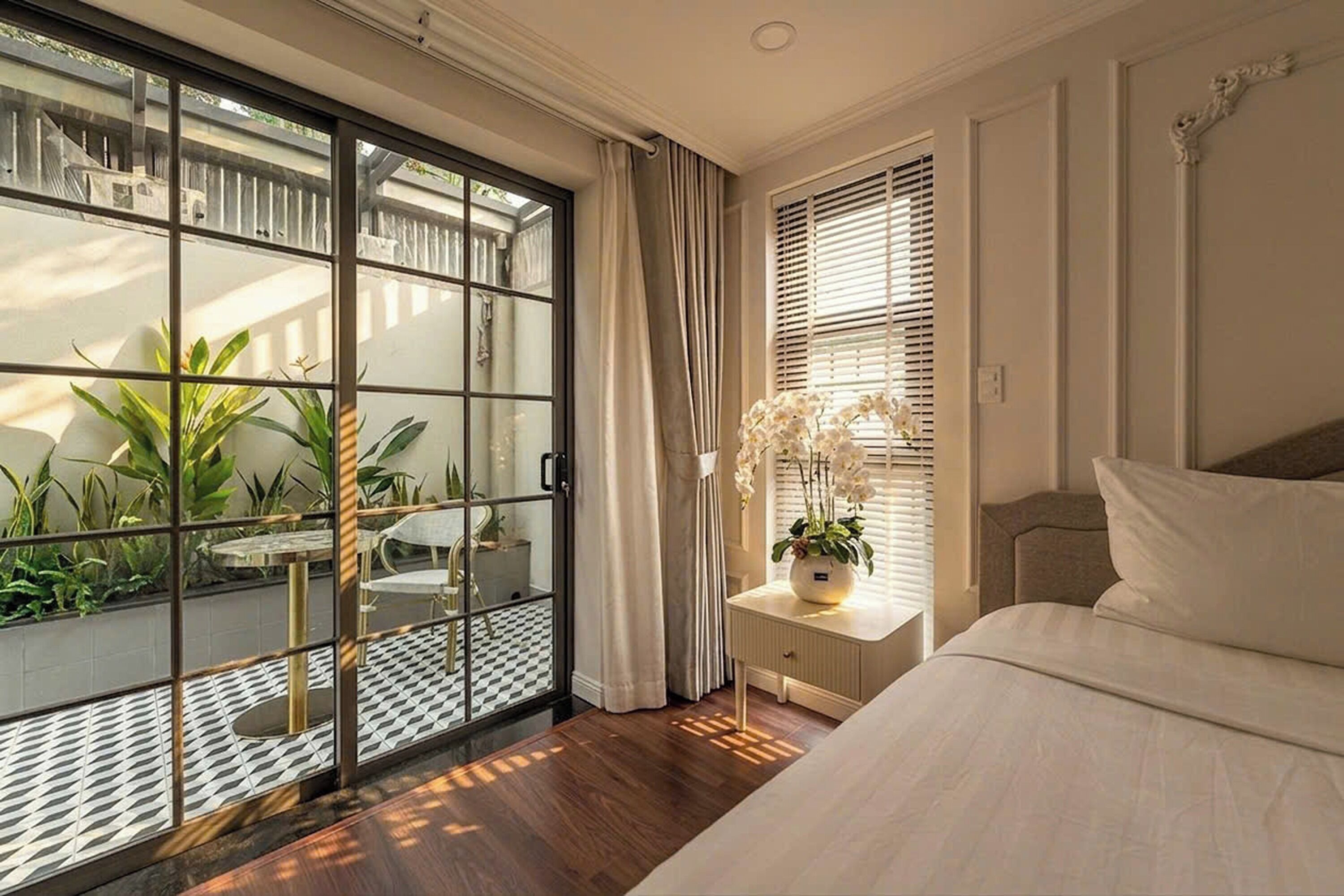 A bedroom with a large sliding glass door leading to a balcony with plants and a dining table.