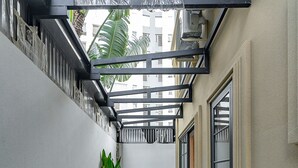 A narrow corridor with a checkered floor, a row of green plants, and a wooden chair. - Golden Sun Apartment & Hotel (Ho Chi Minh City)