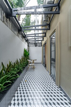 Un couloir étroit au sol à carreaux, une rangée de plantes vertes et une chaise en bois.