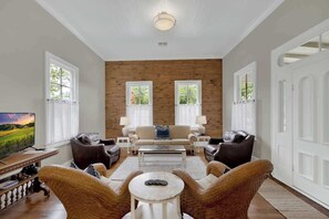 A spacious living room with a wooden accent wall, a sofa set, two armchairs, a coffee table, and a TV on a wooden stand. - The Homestead Estate (Fredericksburg)