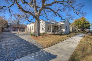 A two-story house with a porch, a driveway, and a large tree in the foreground. - The Homestead Estate (Fredericksburg)