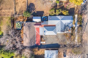 An aerial view of a residential property with a distinct geometric roof design, a fenced yard, and a small patio area. - The Homestead Estate (Fredericksburg)