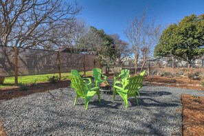 A patio area with four green Adirondack chairs arranged around a small fire pit. - The Homestead Estate (Fredericksburg)