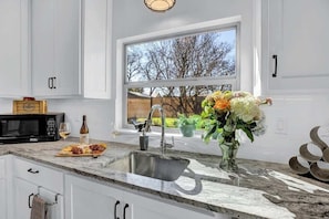 A kitchen with a large window, a sink, a microwave, and a countertop with a bottle and a glass.