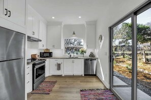 A modern kitchen with white cabinets, stainless steel appliances, and a large window offering a view of the outdoors. - The Homestead Estate (Fredericksburg)