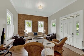 A spacious living room with a wooden accent wall, two windows, a sofa, a coffee table, and a TV.