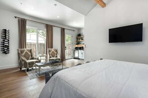A spacious bedroom with a large bed, a flat-screen TV mounted on the wall, and a sliding glass door leading to a balcony. - The Homestead Estate (Fredericksburg)