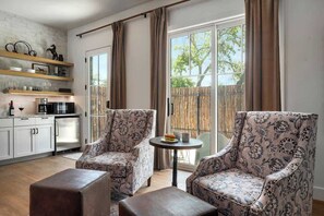A modern living room with two patterned armchairs, a small round table, and a kitchen area with white cabinets and a coffee machine. - The Homestead Estate (Fredericksburg)