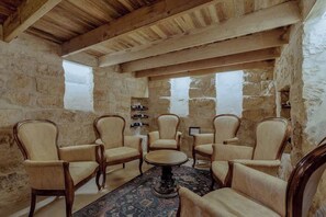 A rustic room with stone walls, wooden beams, and six upholstered chairs around a round table.