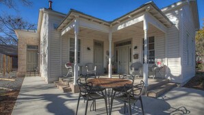 Una casa a due piani con un portico coperto e una zona pranzo con sedie in metallo e un tavolo di legno.