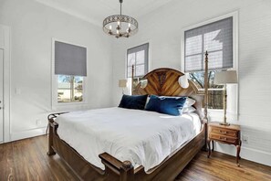 A bedroom with a wooden bed, white bedding, and a chandelier. - The Homestead Estate (Fredericksburg)