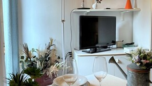 A dining area with a table set for two, a television on a stand, and decorative plants. - Romantic Nest Florence Studio (Firenze)