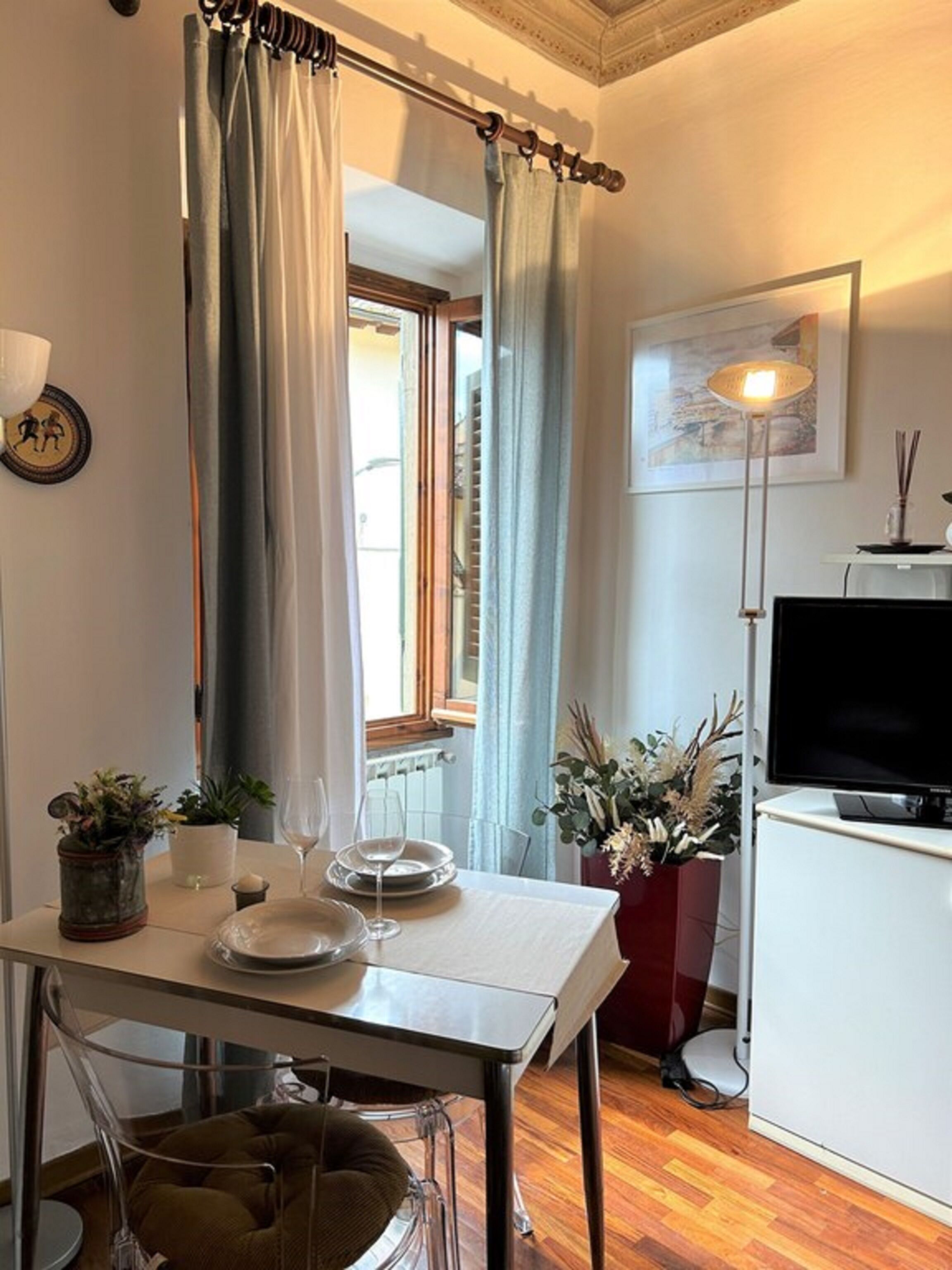 Ein Essbereich mit Tisch für zwei Personen, einem Fernseher und einem fenster mit Vorhängen.