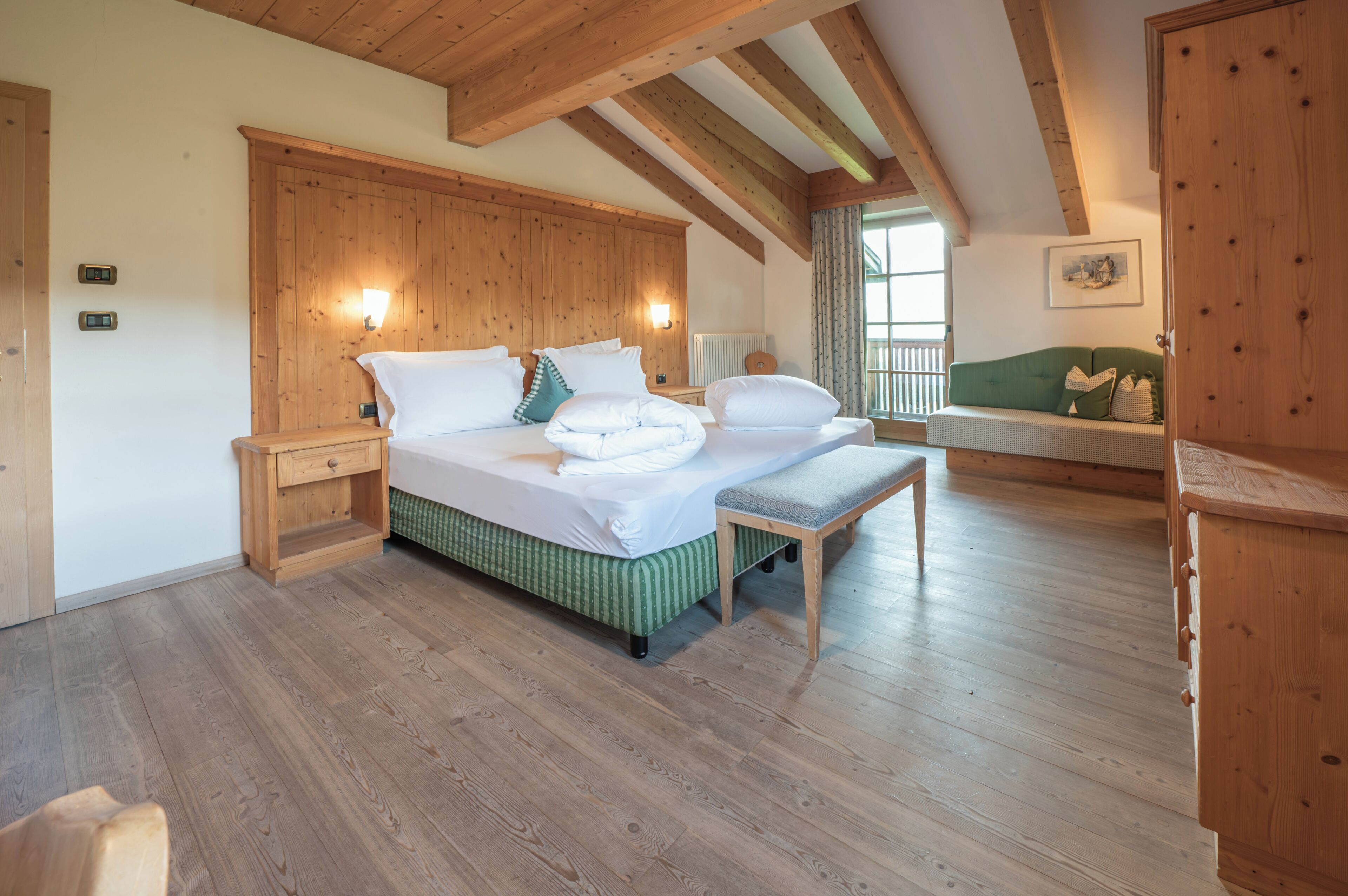 Una camera da letto con soffitto in legno, un letto con lenzuola bianche, una panca e un divano verde.