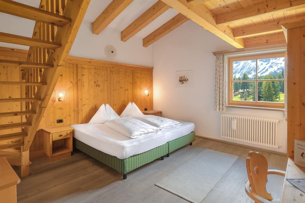 Une chambre dans une cabane en bois, avec un lit, une table de chevet, une chaise, une fenêtre donnant sur les montagnes et un escalier en bois.
