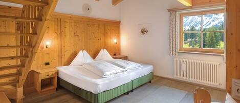 Habitación de cabaña de madera con cama, mesita de noche, silla, ventana con vistas a la montaña y una escalera de madera.