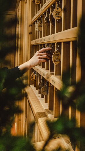 A hand reaching for a key on a wooden rack with numbered slots, likely in a hotel or similar establishment.