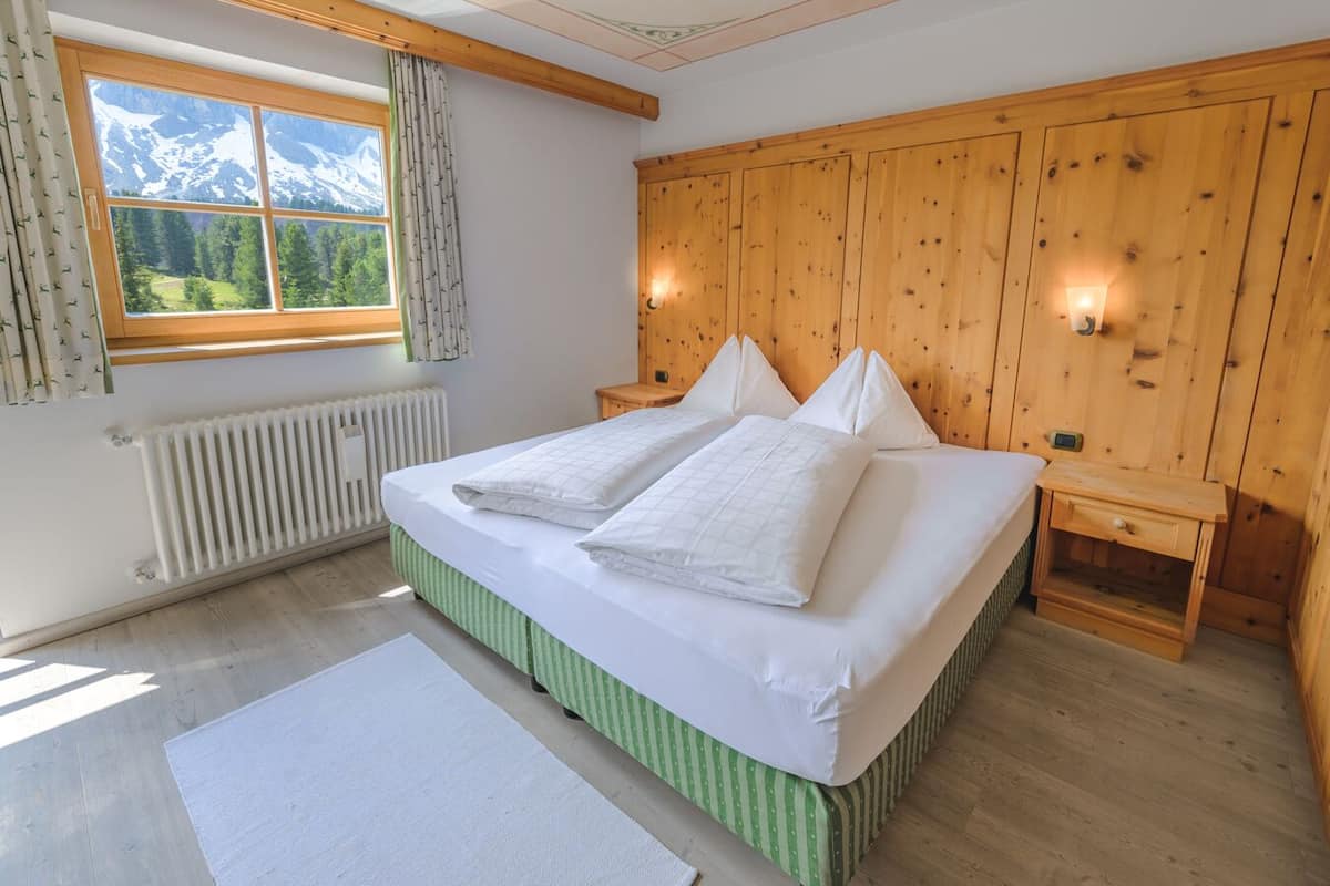 Une chambre à coucher avec une tête de lit en bois, une grande fenêtre donnant sur les montagnes, un radiateur et une table de chevet.