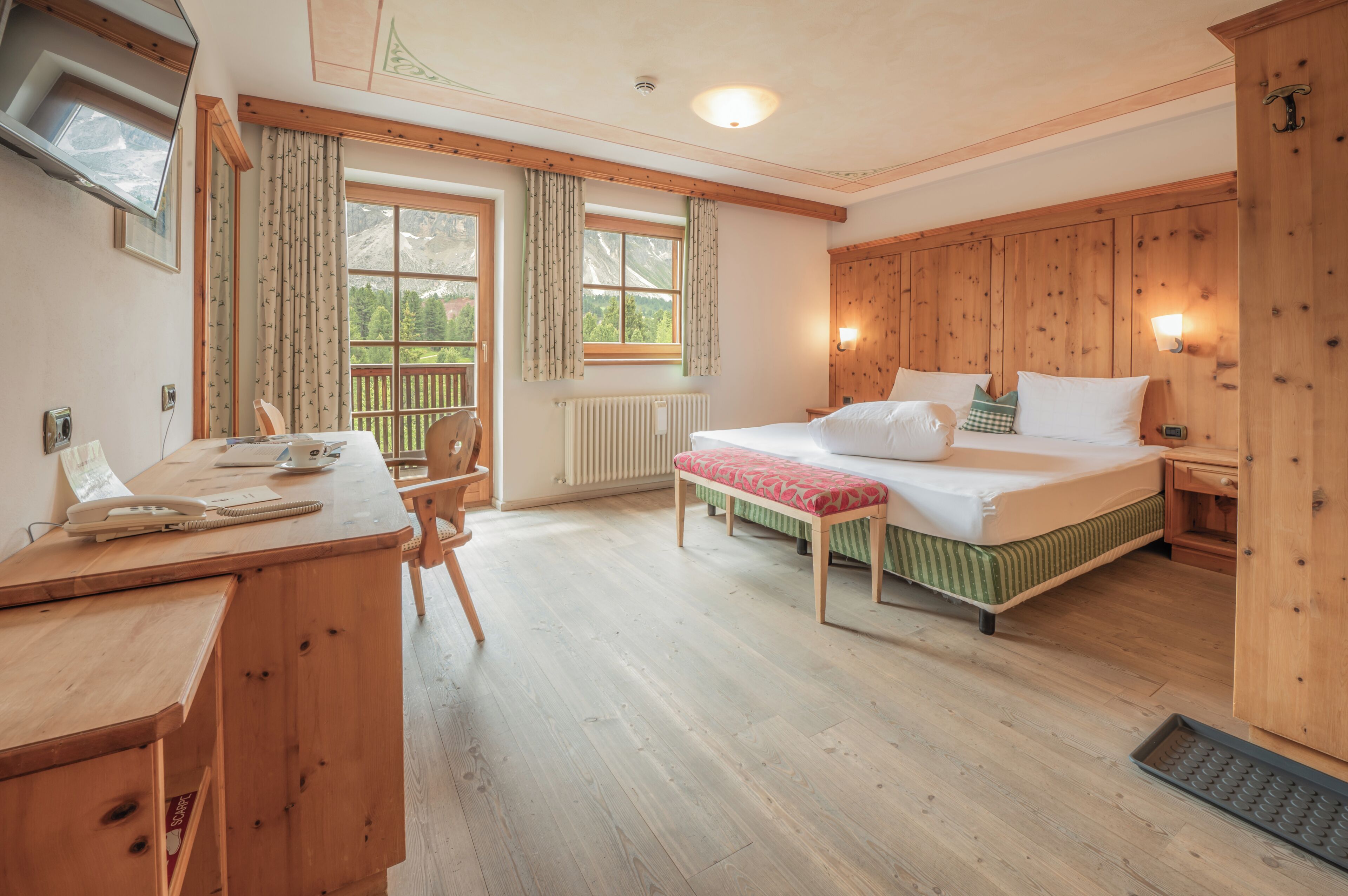 A room with a bed, a desk, a chair, a window with curtains, a radiator, and a wooden cabinet.