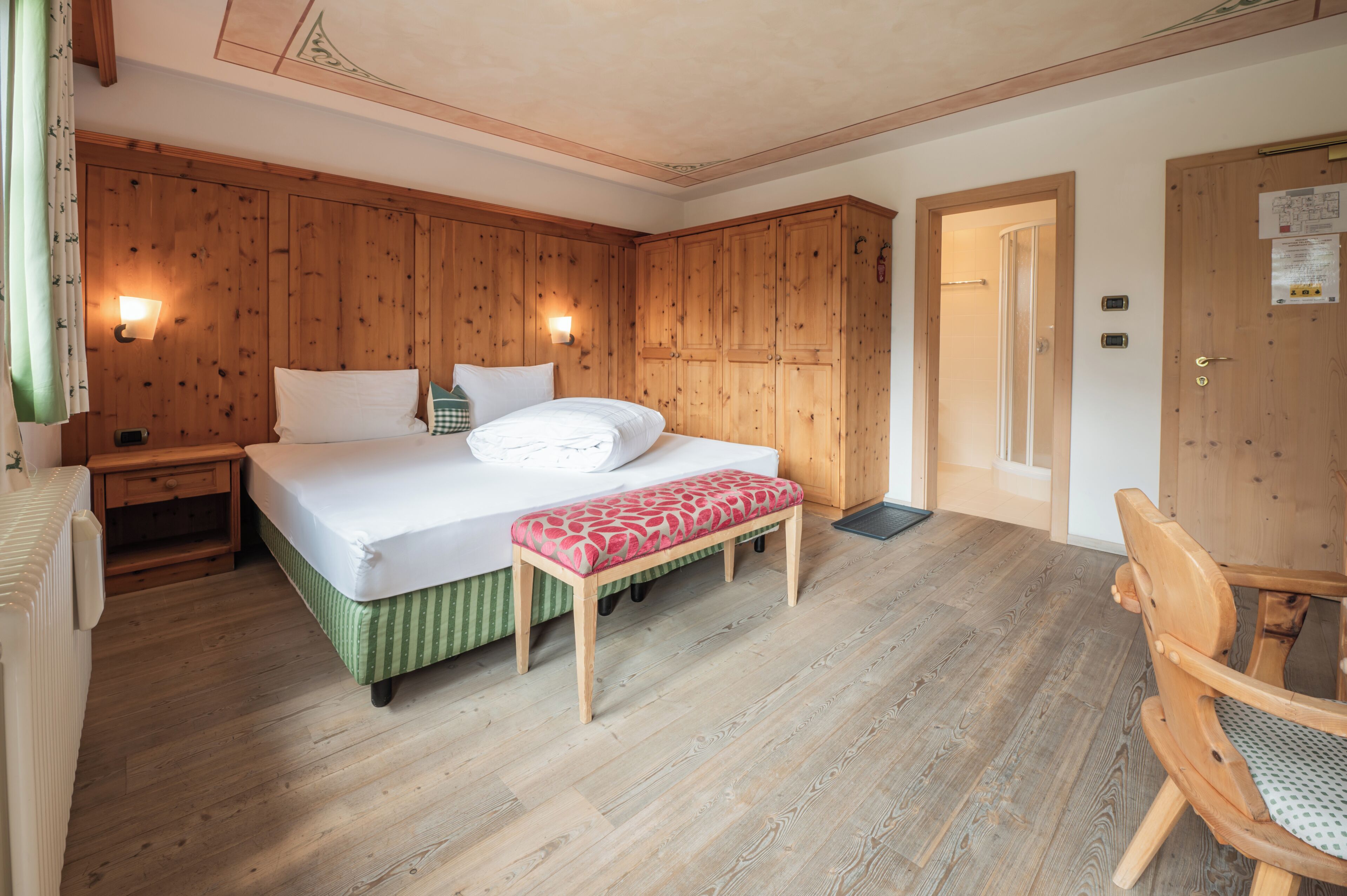 A bedroom with a wooden bed, a bench, a nightstand, and a wooden wardrobe.
