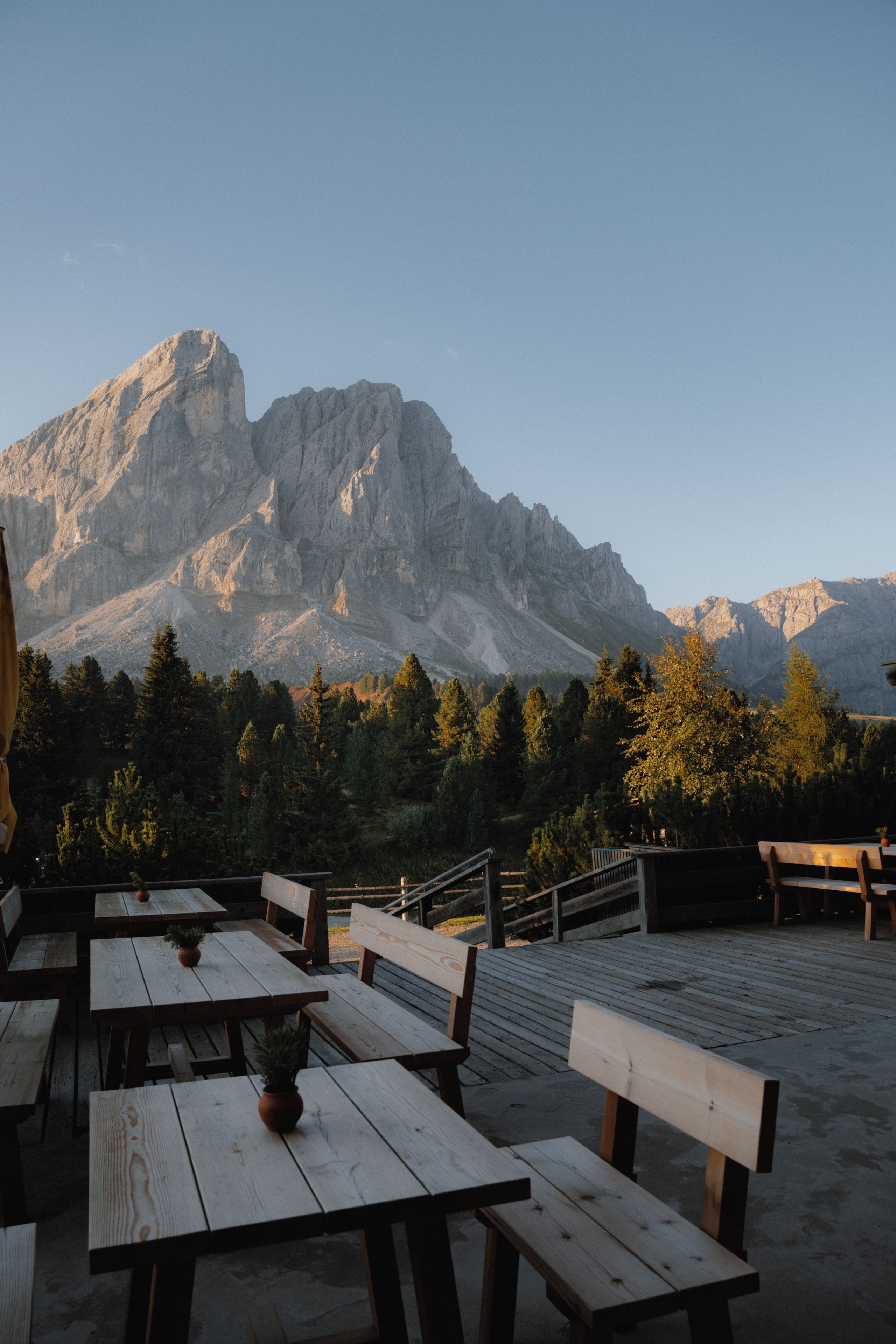 A wooden deck with benches and tables, overlooking a mountainous landscape.