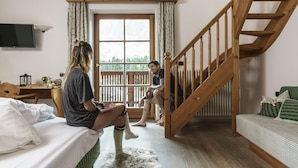 A room with a bed, a wooden staircase, a window with curtains, and a television on the wall. - Ütia de Börz Mountain Lodge (San Martino in Badia)