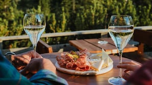 A wooden table with a plate of food and two glasses of white wine, set against a mountainous backdrop. - Ütia de Börz Mountain Lodge (San Martino in Badia)