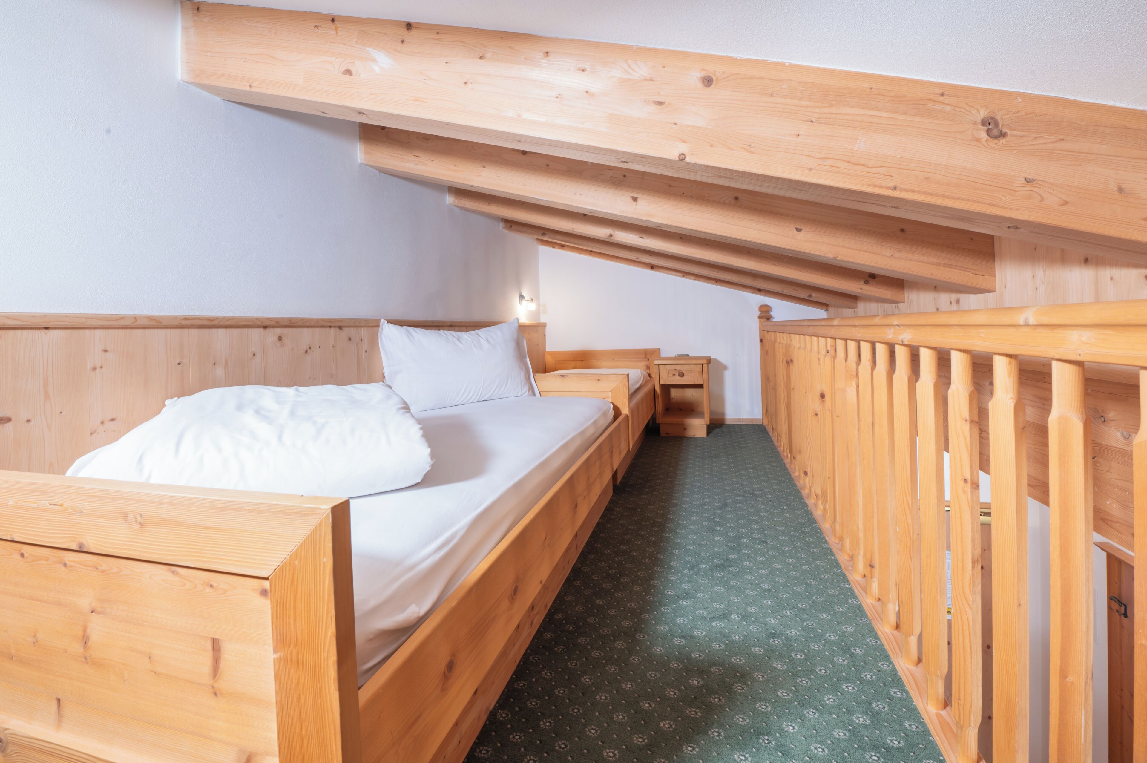 A wooden bunk bed room with a green patterned carpet and a wooden railing.