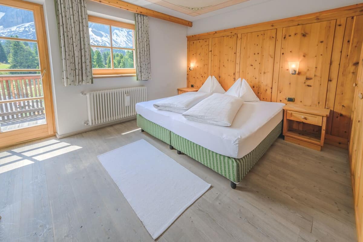 Une chambre à coucher avec un lit, une fenêtre avec des rideaux, une armoire en bois et une vue sur les montagnes.