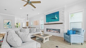 Un salon moderne avec un canapé gris, un fauteuil bleu, une table basse en bois, une cheminée et un ventilateur de plafond.
