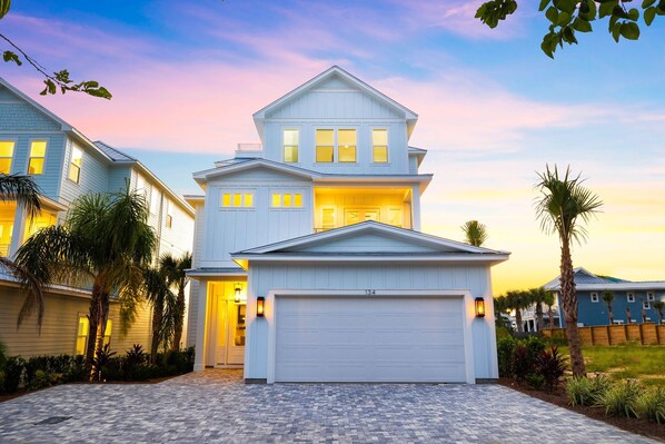 A two-story house with a garage, surrounded by palm trees and a paved driveway.