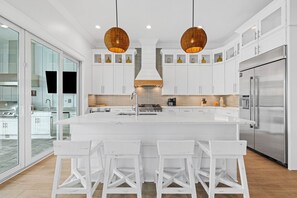 A modern kitchen with a large island, white cabinetry, and stainless steel appliances.