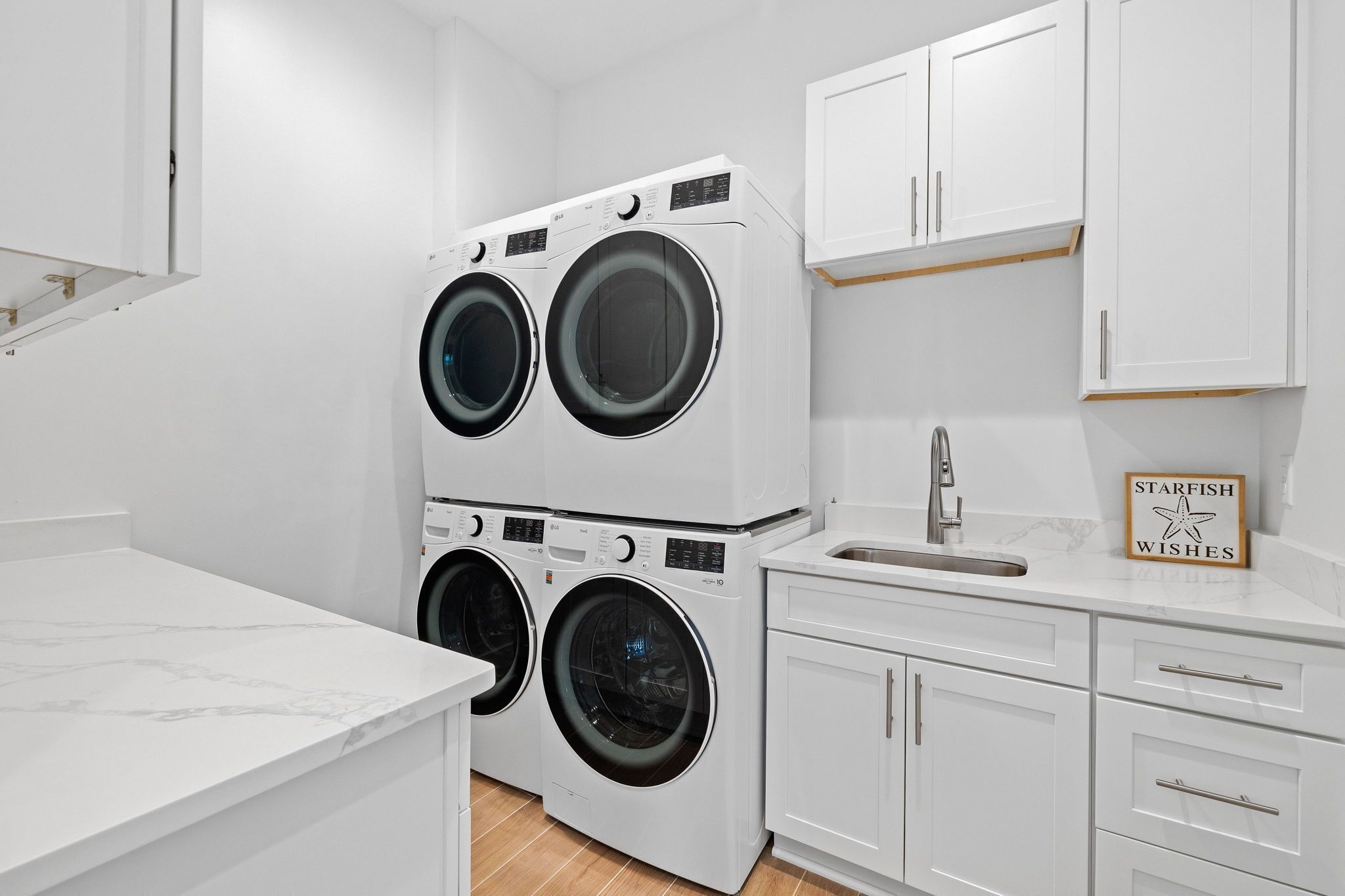 A compact laundry room with two stacked front-loading washing machines, a sink, and a cabinet.