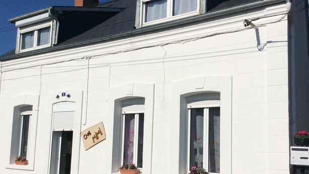 A white building with multiple windows, some with shutters, and a sign on the door. - Gîte Chez Mimi à Anor (Anor)