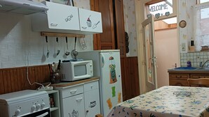 A compact kitchen with a stove, microwave, and refrigerator, wooden cabinets, and a dining area with a table and chairs. - Gîte Chez Mimi à Anor (Anor)