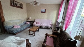 A living room with a sofa, a small table, a chair, and a television. - Gîte Chez Mimi à Anor (Anor)