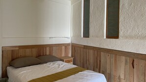 A bedroom with a wooden headboard, a bed with white bedding and a green throw, a nightstand, and a wall-mounted light fixture. - Casa Calamar Zihuatanejo (Gro)