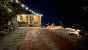 A building with a stone pathway leading to a door, surrounded by string lights and a red path. - Casa Calamar Zihuatanejo (Gro)