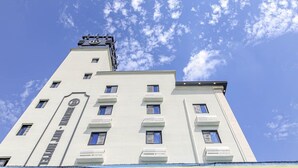 Un edificio alto y blanco con múltiples ventanas y una torre distintiva con un logotipo en la parte superior.