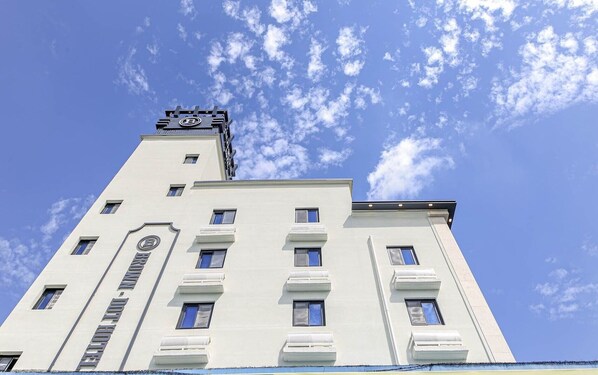 A tall, white building with multiple windows and a distinctive tower with a logo at the top. - Brown Dot Hotel Sinan (Gwangju)