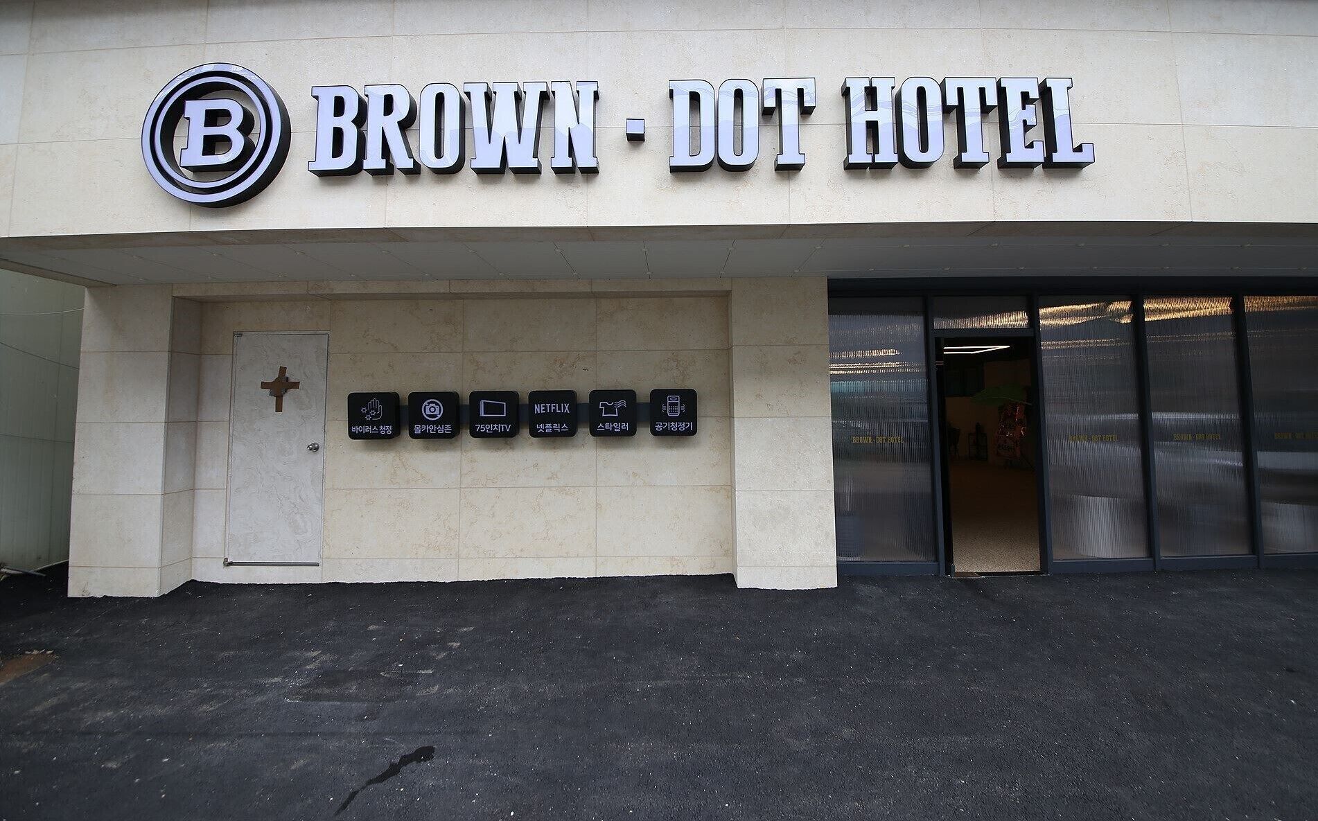 El exterior del Hotel Brown-Dot con un cartel que muestra servicios como lavado de manos, servicio de lavandería, NETFLIX y una tienda 7-Eleven.