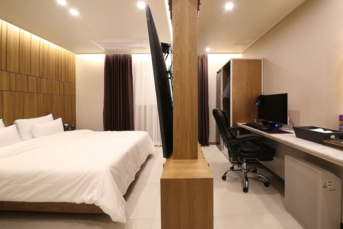 Habitación de hotel con cama, escritorio con computadora, silla y un grueso pilar de madera.