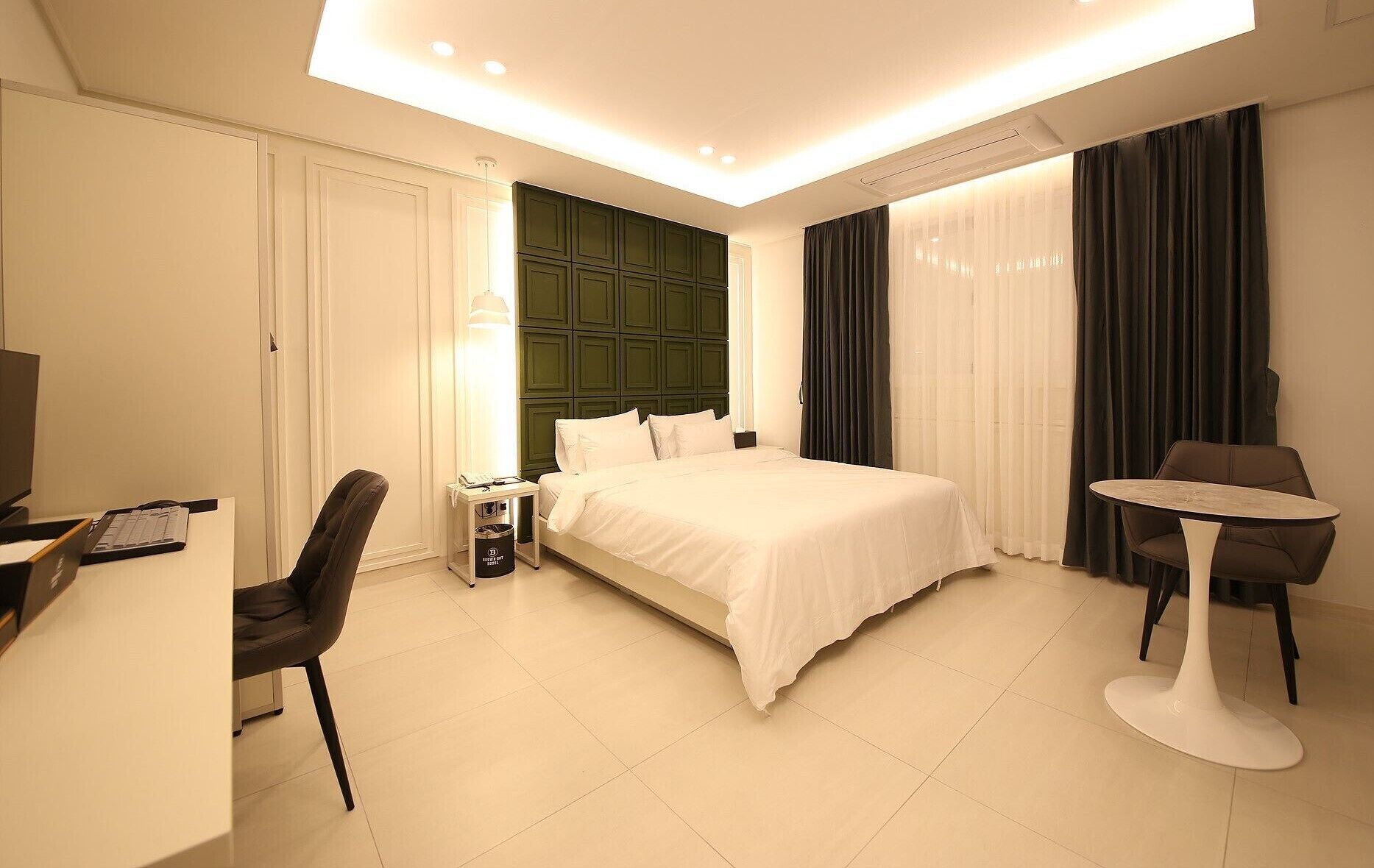 A hotel room with a bed, a desk with a computer, a chair, a small table, and a TV.