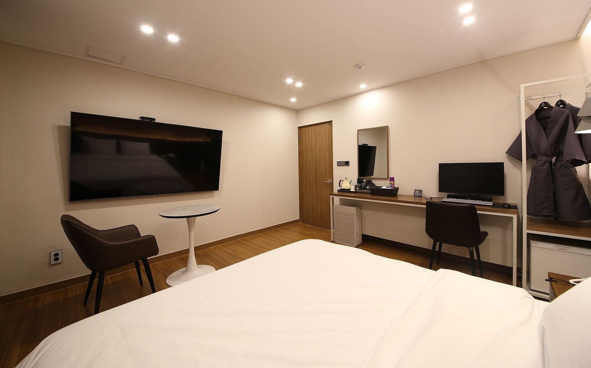 Habitación de hotel con cama, escritorio con computadora, televisión, silla y perchero para bata.