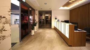 Zona de recepción de un hotel con un mostrador de madera, un televisor y una planta en maceta.